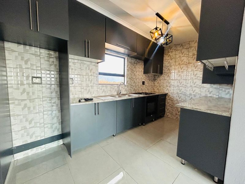 Modern kitchen featuring dark grey cabinetry, stone countertops, tiled splashbacks, built-in oven and hob, and contemporary pendant lighting.