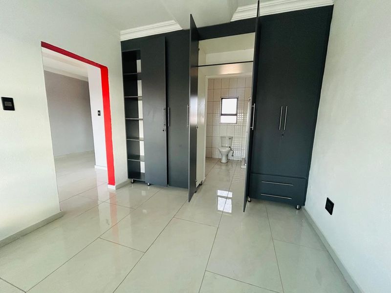 A bright bedroom featuring modern tiled flooring, built-in dark cabinetry, and direct access to an en-suite bathroom.