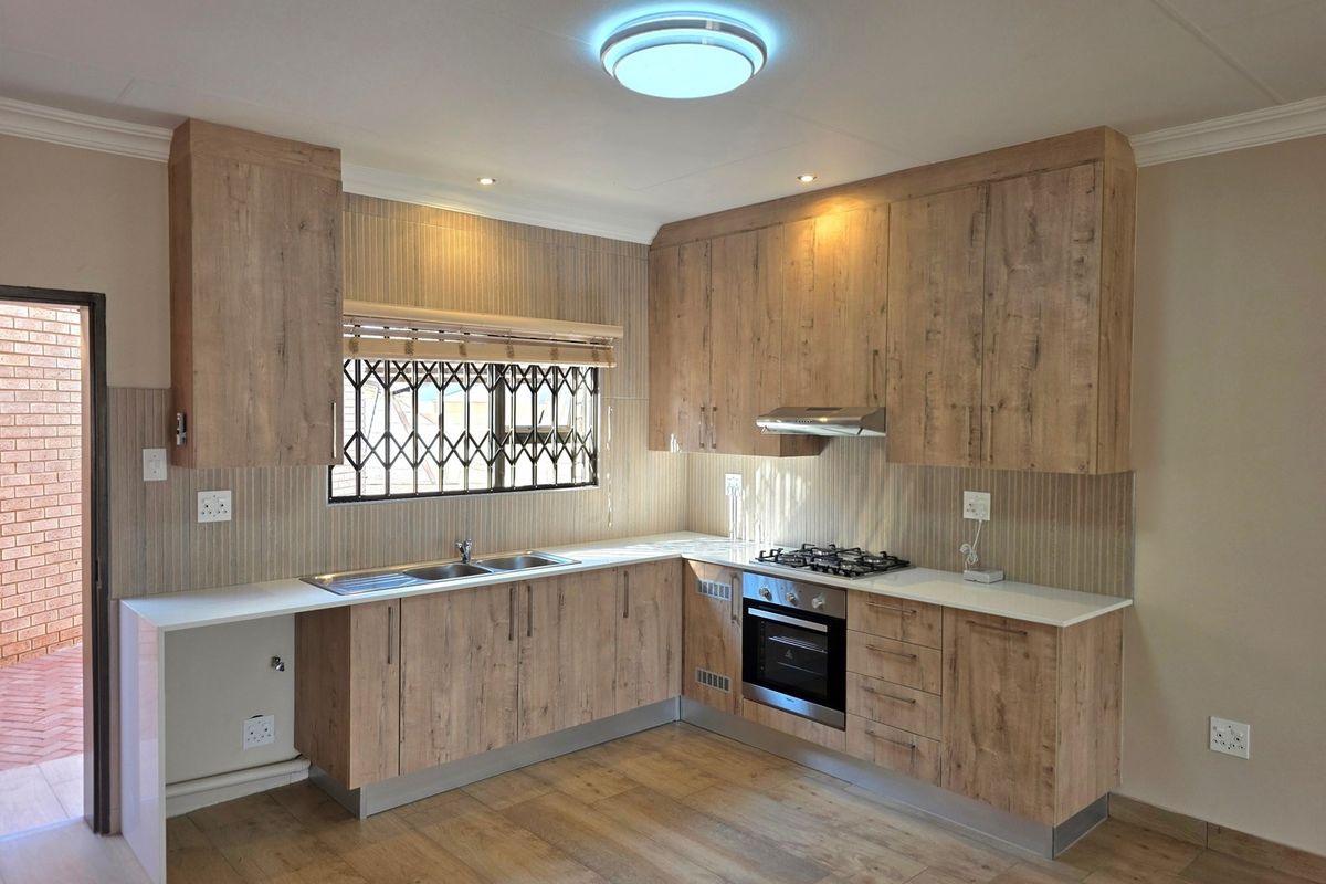 Modern kitchen featuring wood-look cabinetry, built-in oven, gas hob, extractor fan, and a stainless steel sink with direct access to an outdoor area.