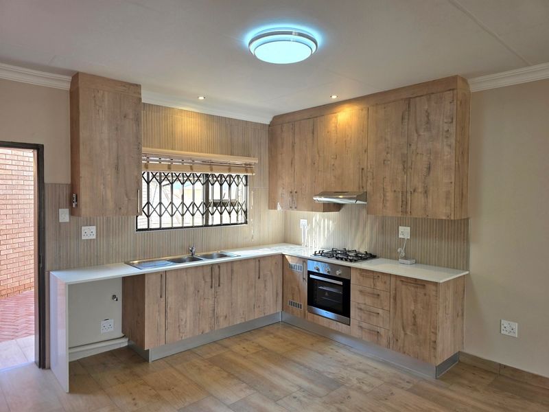 Modern kitchen featuring wood-look cabinetry, built-in oven, gas hob, extractor fan, and a stainless steel sink with direct access to an outdoor area.