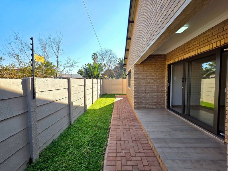 Rear exterior view of the townhouse featuring a brick facade, paved patio area, small lawn, and secure boundary wall with electric fencing.