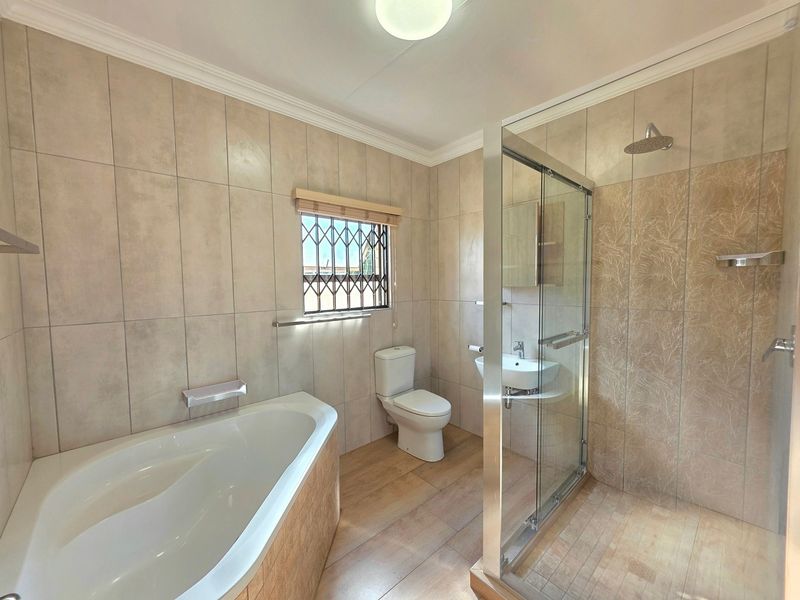 A clean, modern bathroom featuring a built-in bathtub, a separate glass-enclosed shower, a toilet, and a wall-mounted basin with neutral tiled finishes.