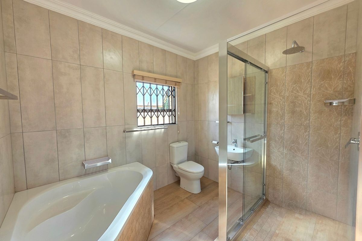 A clean, modern bathroom featuring a built-in bathtub, a separate glass-enclosed shower, a toilet, and a wall-mounted basin with neutral tiled finishes.