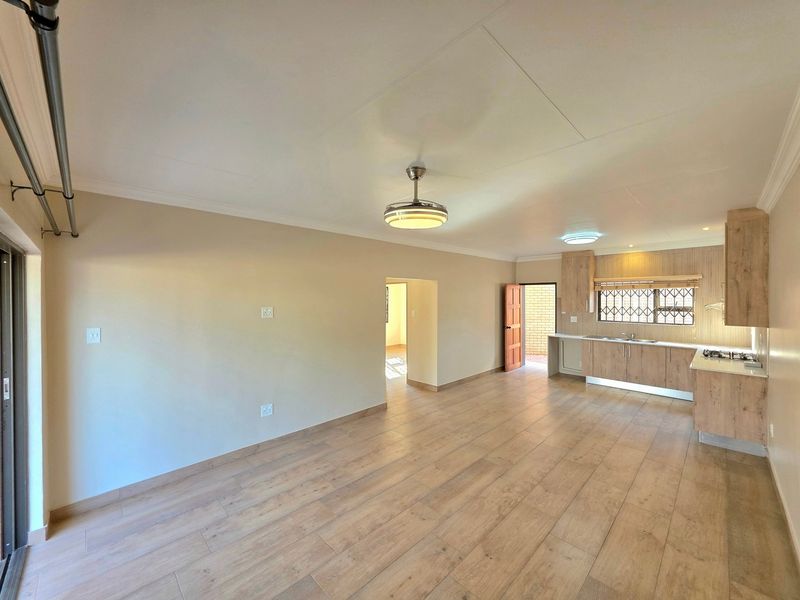 Spacious open-plan living area featuring modern laminate flooring, a ceiling fan, and a functional kitchen with built-in cabinetry and a hob.