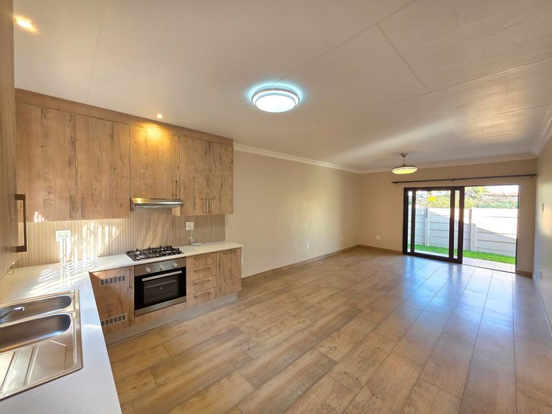 Spacious open-plan living area featuring a modern kitchen with wood-finish cabinetry, built-in appliances, and direct access to the rear garden via sliding doors.