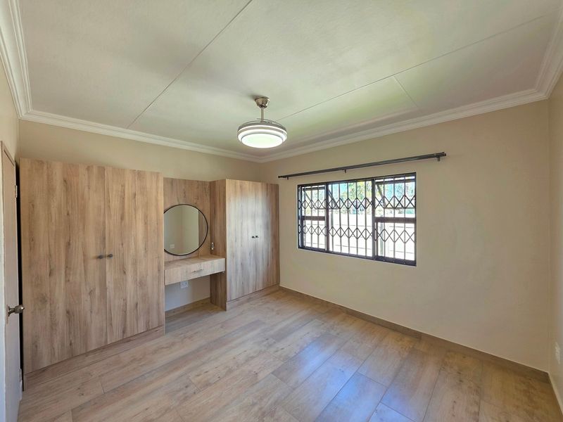 A bright bedroom featuring modern wood-look laminate flooring, built-in cupboards with an integrated vanity, and a security gate on the window.