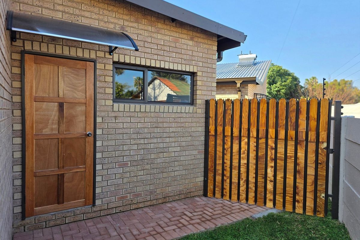 A well-maintained rear exterior view featuring a brick facade, a wooden door with a modern awning, and a secure wooden fence.