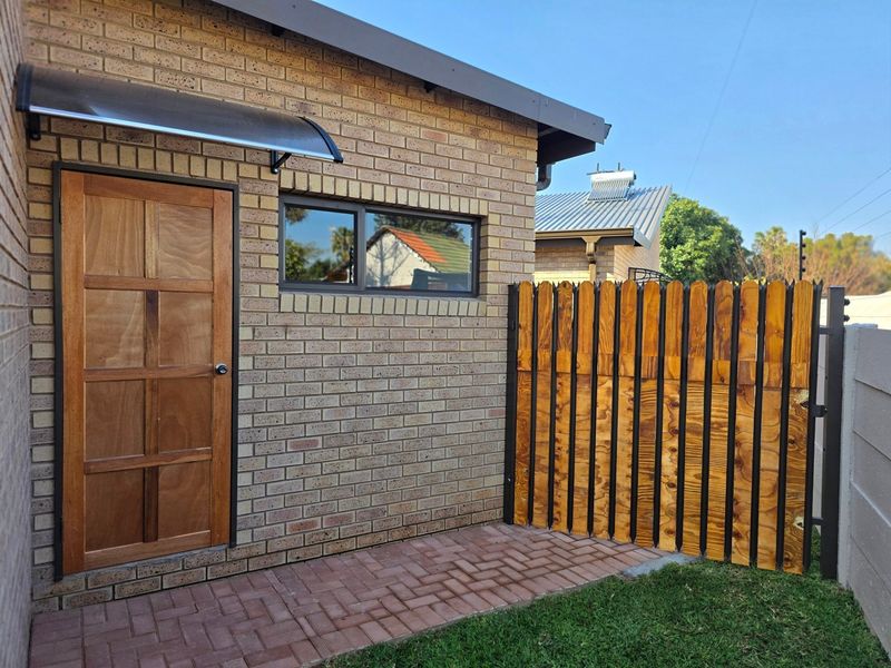 A well-maintained rear exterior view featuring a brick facade, a wooden door with a modern awning, and a secure wooden fence.
