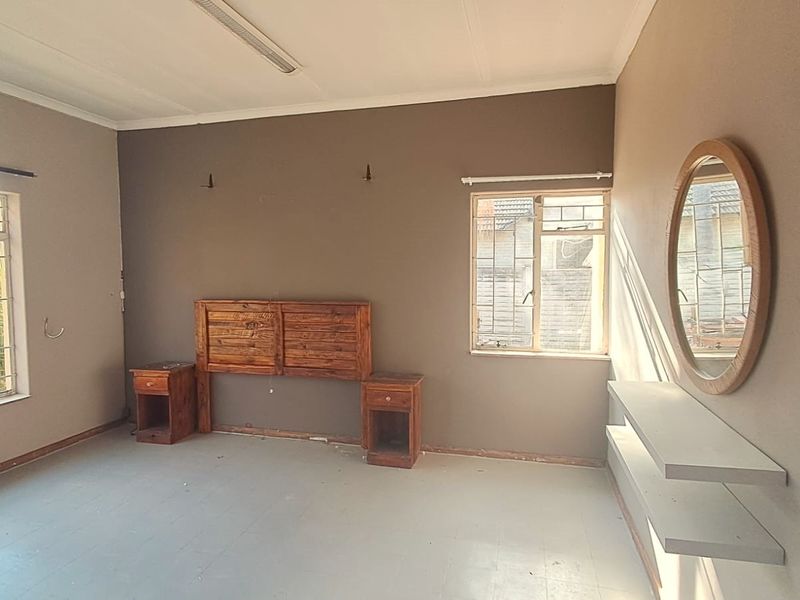 Spacious bedroom featuring built-in headboard, bedside tables, and floating shelves, with natural light provided by dual windows with security bars.