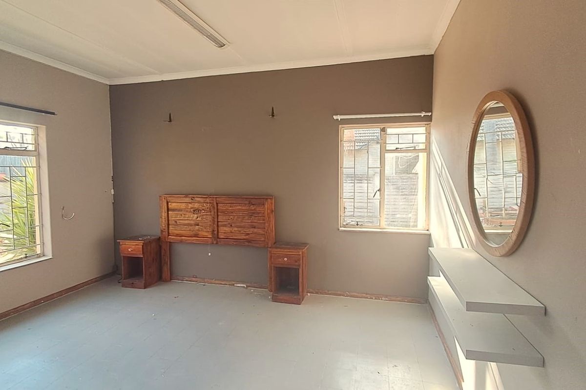 Spacious bedroom featuring built-in headboard, bedside tables, and floating shelves, with natural light provided by dual windows with security bars.