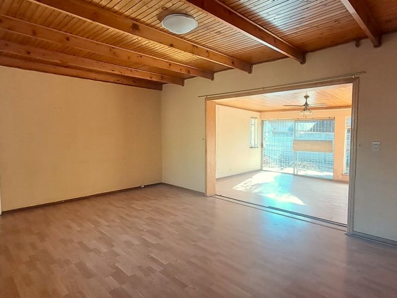 Spacious living area featuring exposed timber beam ceilings, laminate flooring, and a large sliding door leading to an adjacent sunroom or patio space.