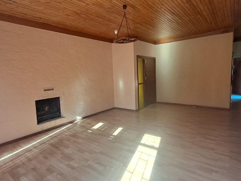 Spacious living room featuring a wood-paneled ceiling, laminate flooring, and a built-in fireplace, offering a blank canvas for renovation.