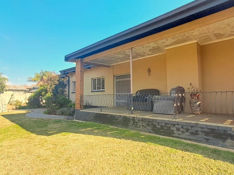 A covered patio area featuring brick pillars, wrought iron railings, and tiled flooring, overlooking a spacious rear garden.