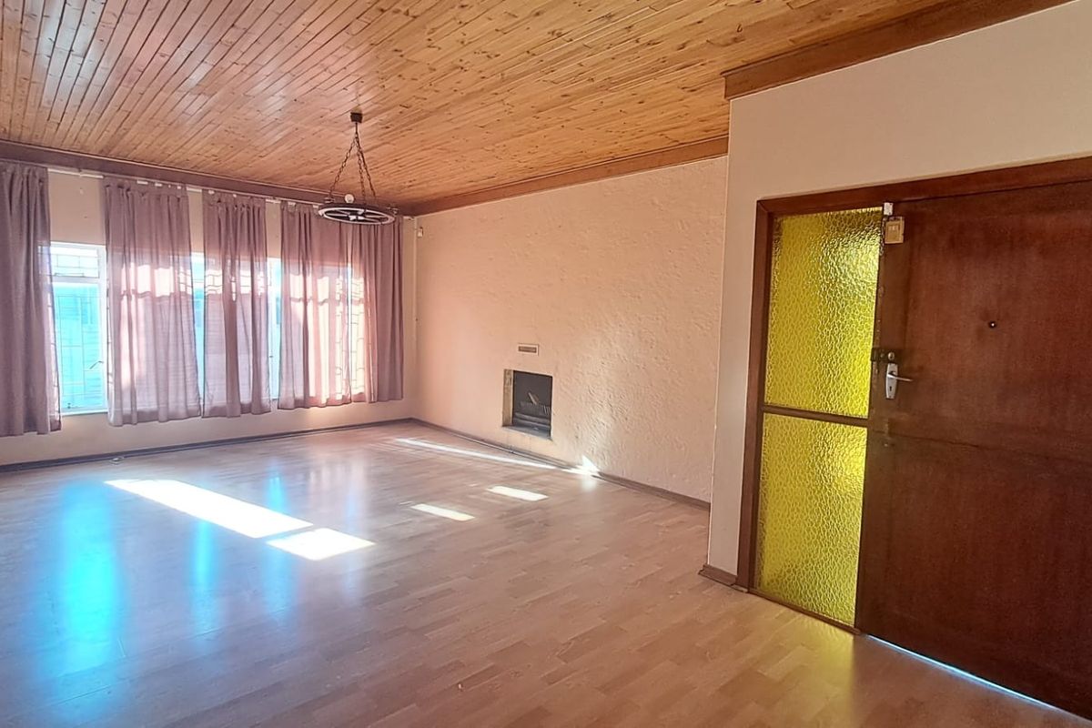 Spacious living room featuring a timber-clad ceiling, laminate flooring, and a built-in fireplace, offering a blank canvas for renovation.