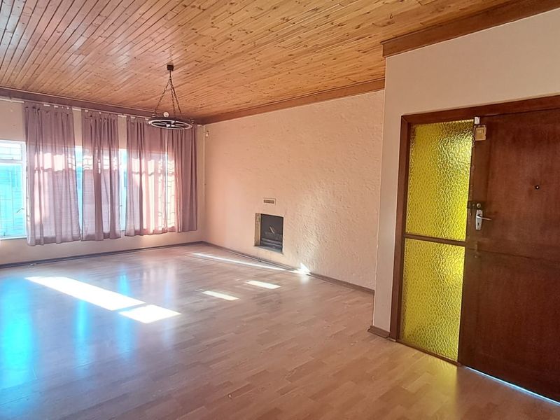 Spacious living room featuring a timber-clad ceiling, laminate flooring, and a built-in fireplace, offering a blank canvas for renovation.