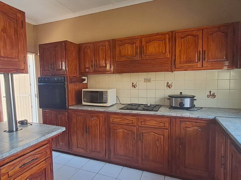 A functional kitchen featuring traditional wooden cabinetry, laminate countertops, a built-in oven, and a gas hob with a tiled backsplash.