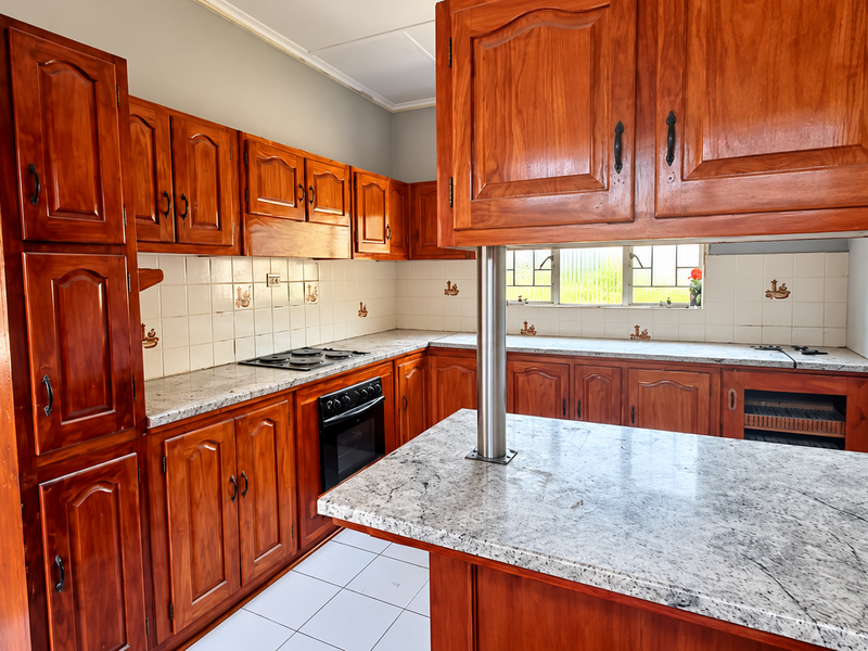 A spacious kitchen featuring traditional wooden cabinetry, granite countertops, a built-in oven and hob, and a functional breakfast bar area.