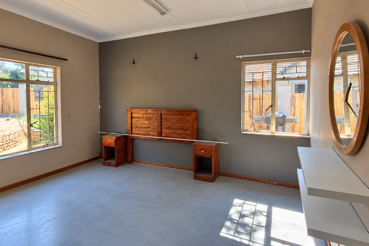 A spacious bedroom featuring neutral walls, tiled flooring, built-in wooden headboard with bedside tables, and floating shelves.