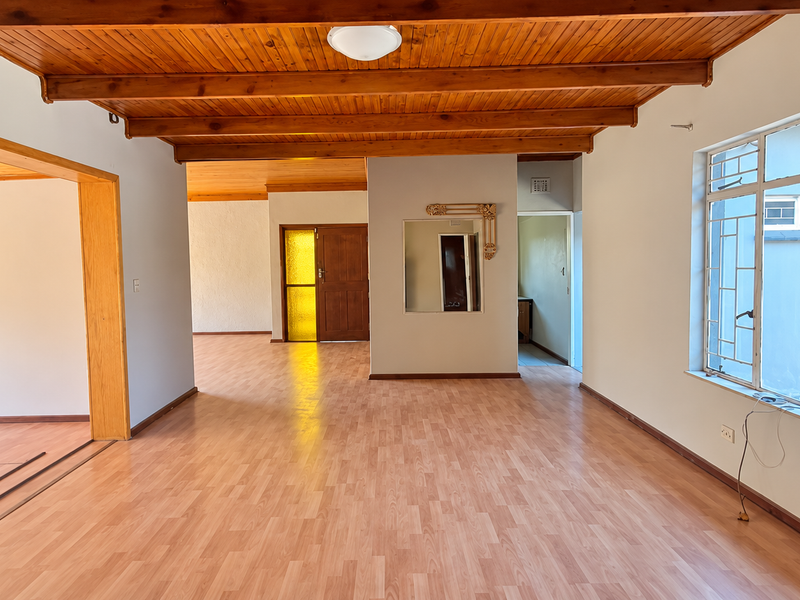Spacious open-plan living area featuring exposed timber ceiling beams, laminate flooring, and large steel-framed windows, offering a bright and versatile blank canvas.