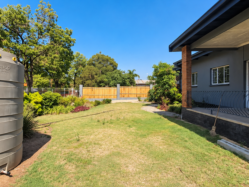 Spacious rear garden featuring a large water storage tank, a covered patio with wrought iron railings, and secure perimeter fencing.