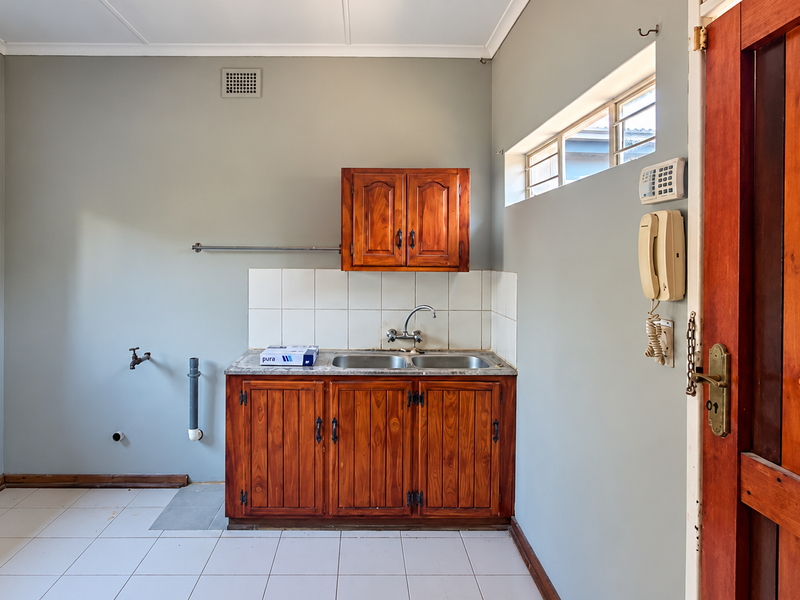 A functional laundry room featuring wooden cabinetry, a double stainless steel sink, tiled flooring, and dedicated plumbing connections for appliances.