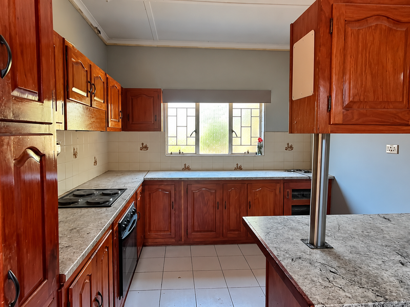 A functional kitchen featuring traditional wooden cabinetry, stone-look countertops, a built-in hob and oven, and a breakfast bar, offering a classic layout.