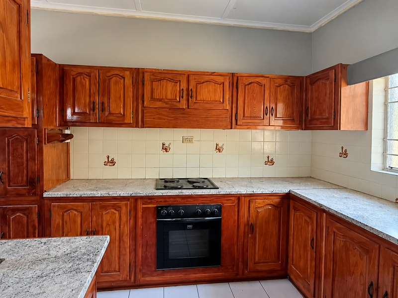 A functional kitchen featuring traditional wooden cabinetry, laminate countertops, a built-in oven, and an electric hob with a tiled backsplash.