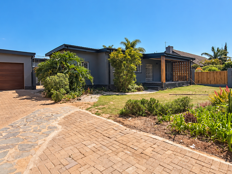 Front exterior view of a house featuring a paved driveway, attached garage, and a covered patio area with established garden landscaping.