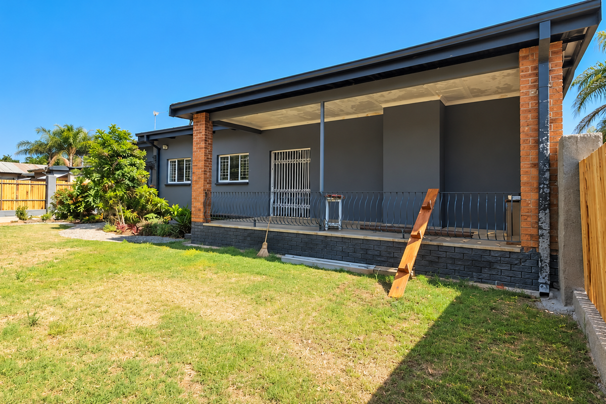 Rear view of the property featuring a covered patio with brick pillars, wrought iron railing, and a spacious garden with timber fencing.