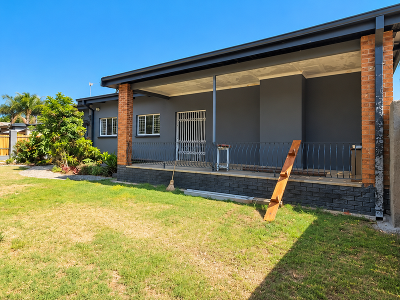 Rear view of the property featuring a covered patio with brick pillars, wrought iron railing, and a spacious garden with timber fencing.