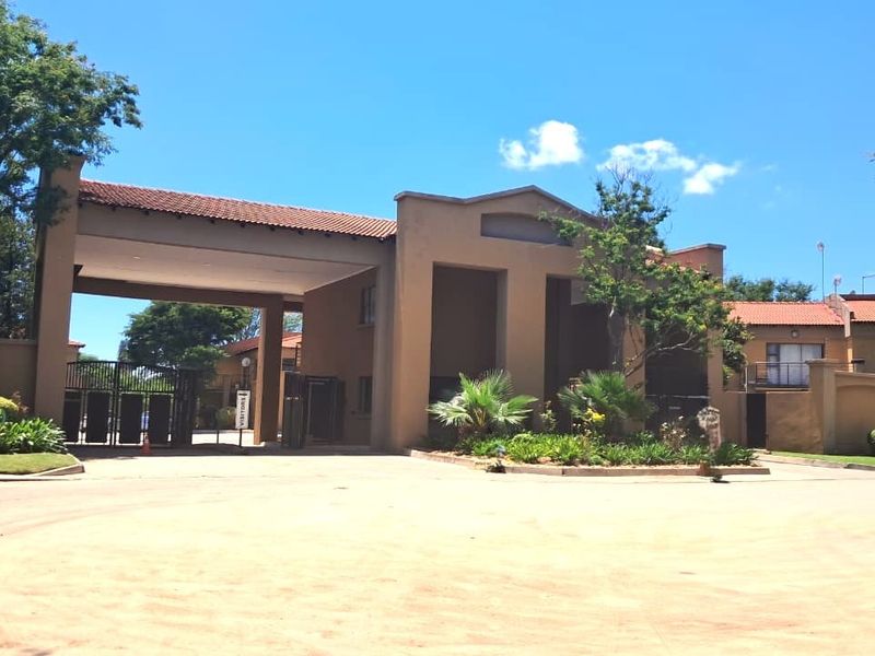 The main entrance to the apartment complex featuring a secure gated access point, paved driveway, and established landscaped garden areas.