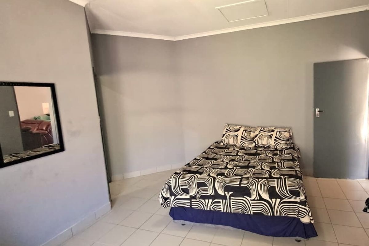 A simple bedroom featuring tiled flooring and neutral grey walls, providing a functional space ready for personalization.