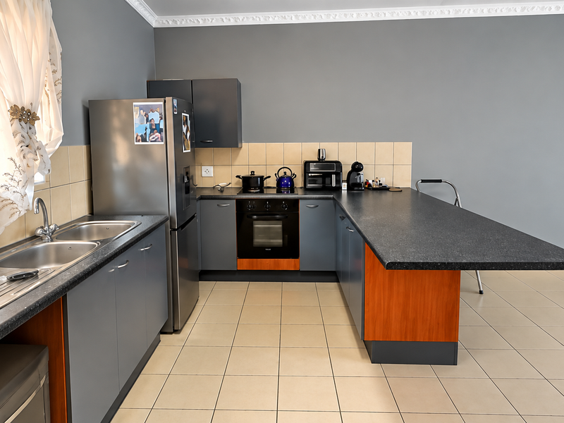 A functional kitchen featuring dark grey cabinetry, a breakfast bar, built-in oven, hob, and a double stainless steel sink with tiled backsplash.