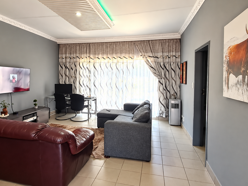 A spacious living room featuring tiled flooring, decorative ceiling cornicing, and a large sliding door providing access to the exterior.