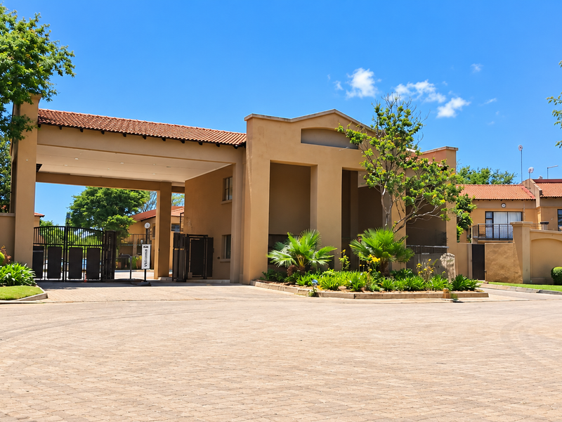 The main entrance to the apartment complex features a secure gated access point, paved driveway, and well-maintained landscaped gardens.