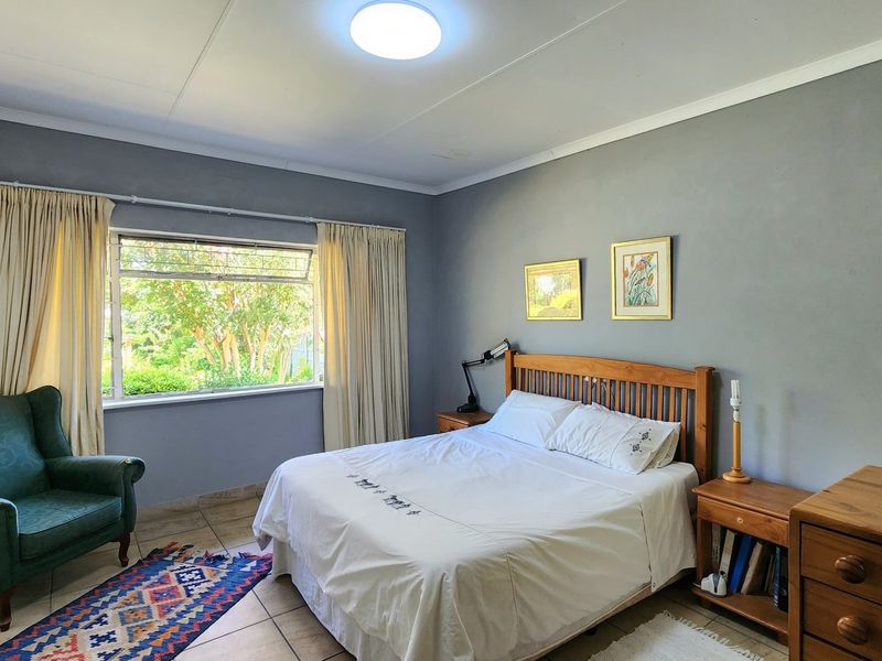 A well-lit bedroom featuring tiled flooring, neutral wall finishes, and a large window providing natural light and garden views.