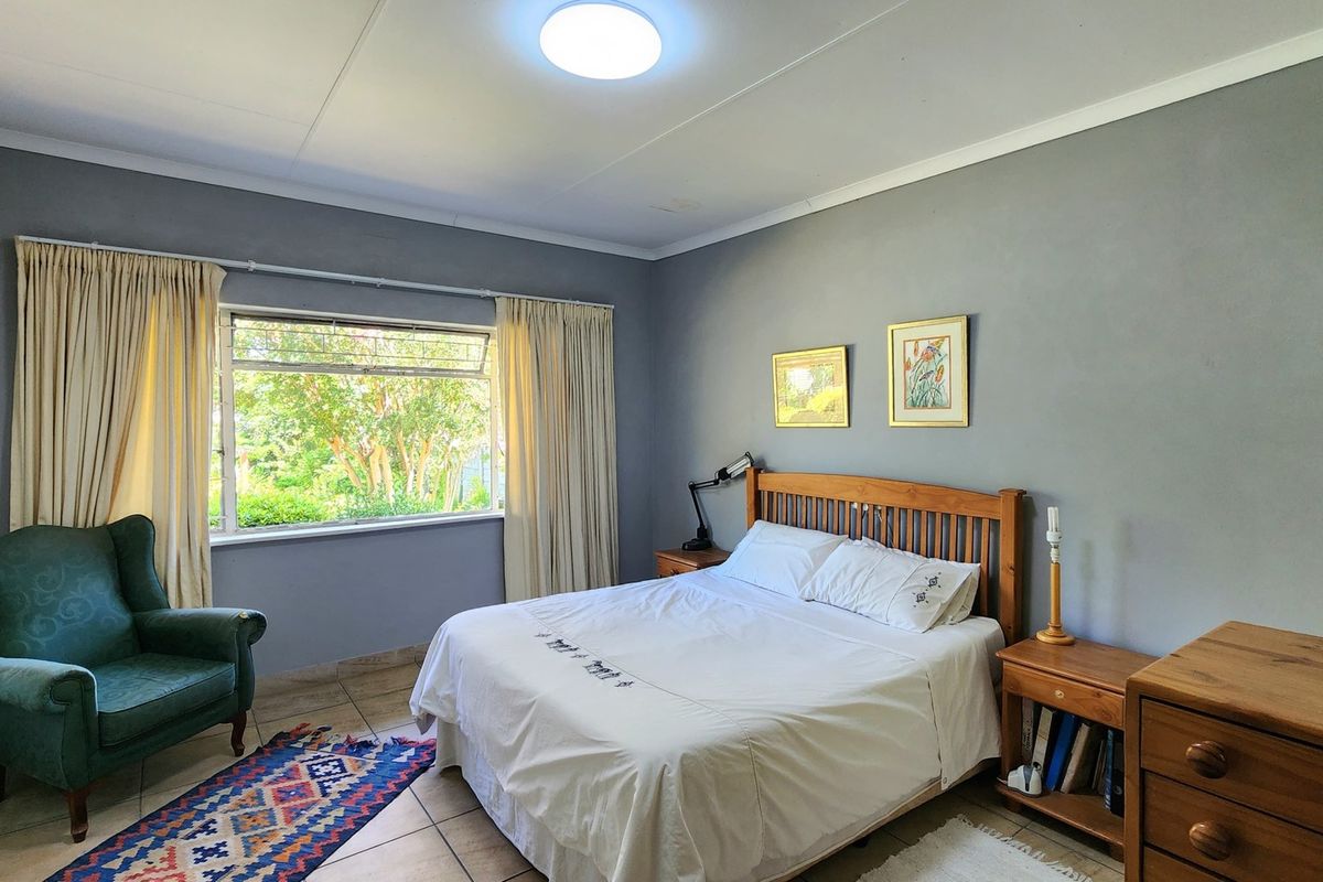 A well-lit bedroom featuring tiled flooring, neutral wall finishes, and a large window providing natural light and garden views.