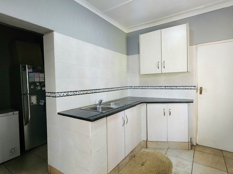 A functional kitchen area featuring white built-in cabinetry, dark laminate countertops, a stainless steel sink, and neutral tiled flooring and backsplash.