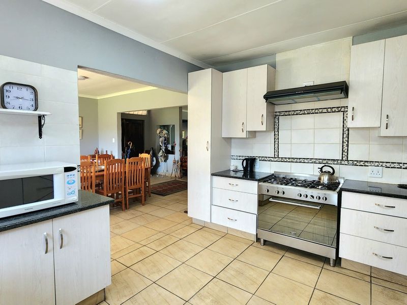 Open-plan kitchen featuring light-toned cabinetry, granite countertops, and a gas stove, flowing into an adjacent dining area with tiled flooring throughout.