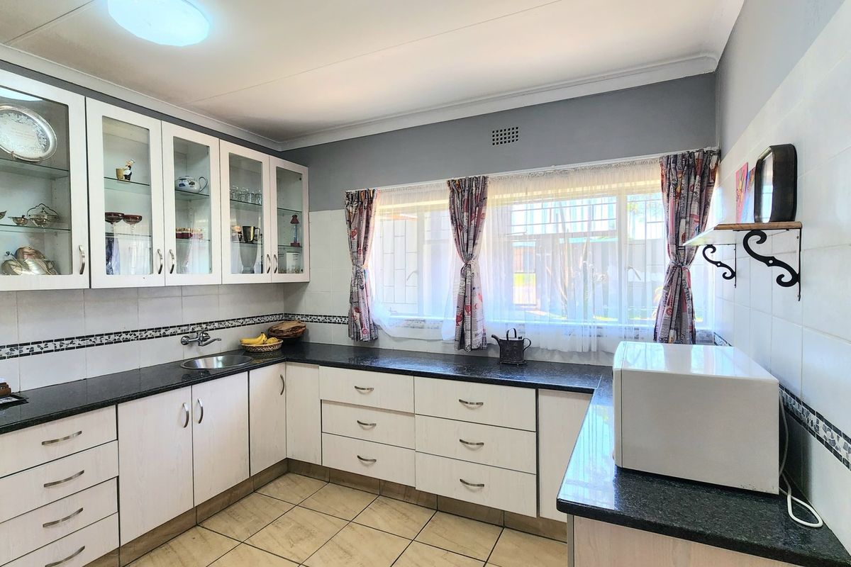 A functional kitchen featuring white cabinetry, dark laminate countertops, tiled backsplash, and ceramic floor tiles with ample natural light.