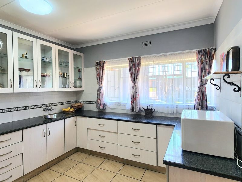 A functional kitchen featuring white cabinetry, dark laminate countertops, tiled backsplash, and ceramic floor tiles with ample natural light.