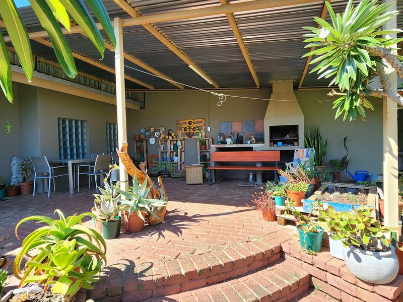 Covered outdoor patio featuring a built-in braai, brick paved flooring, and direct access to the home through a security gate.