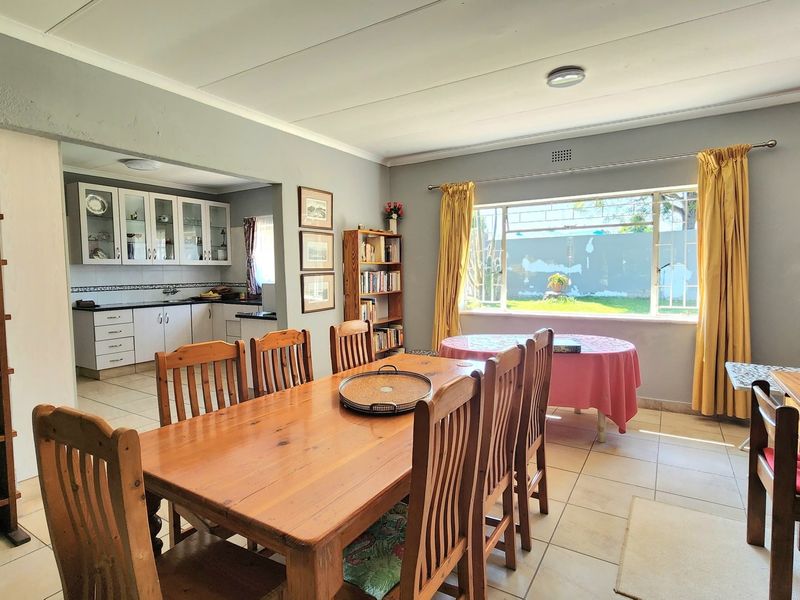 Open plan dining area flowing into a functional kitchen with tiled floors and ample natural light from the large window.