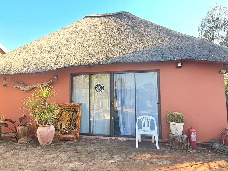 Rear view of a flat featuring a traditional thatch roof, sliding glass doors, and a brick-paved patio area.