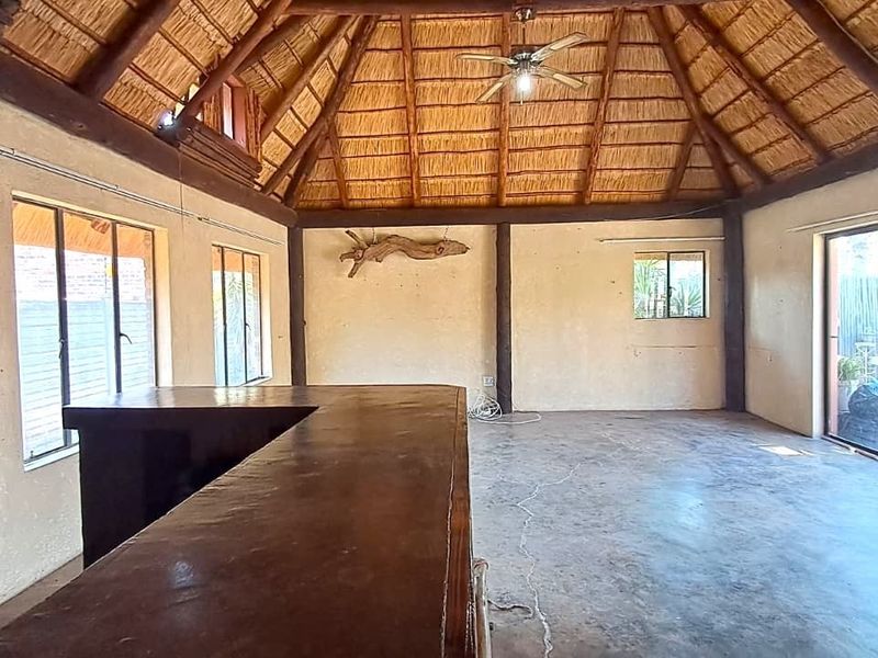 Spacious bar area featuring a high thatched roof with exposed timber beams, concrete flooring, and large sliding glass doors leading to the exterior.