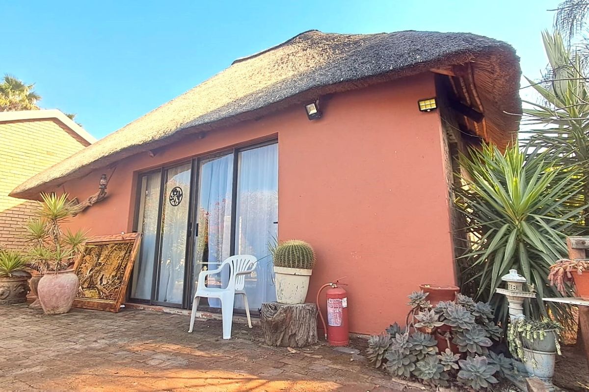 Exterior view of a cottage-style flat featuring a traditional thatch roof, sliding glass doors, and a brick-paved patio area.