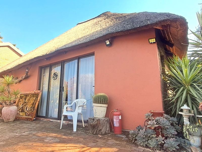 Exterior view of a cottage-style flat featuring a traditional thatch roof, sliding glass doors, and a brick-paved patio area.