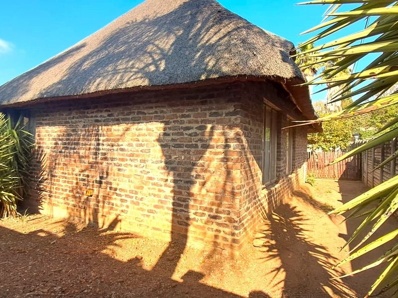 A rear view of a property featuring a traditional thatch roof and exposed brick exterior walls set within a garden area.