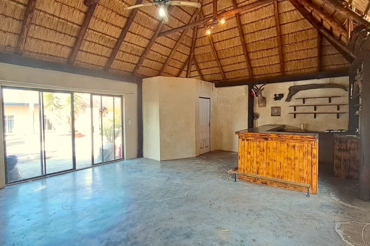 Spacious bar area featuring a traditional thatched roof with exposed timber beams, concrete flooring, and a built-in wooden bar counter.