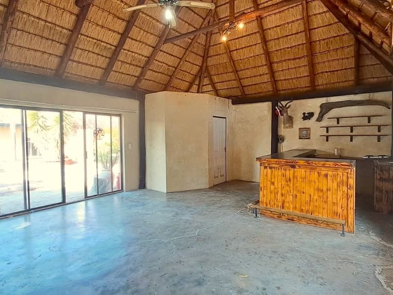 Spacious bar area featuring a traditional thatched roof with exposed timber beams, concrete flooring, and a built-in wooden bar counter.